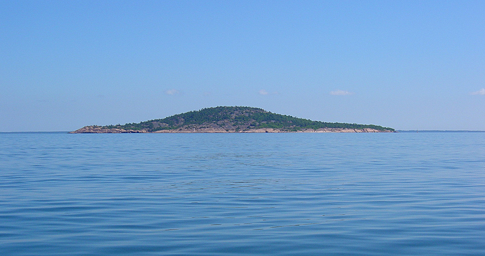 Blå Jungfrun nationalpark fotad från havet. Vattnet är stilla och blått.