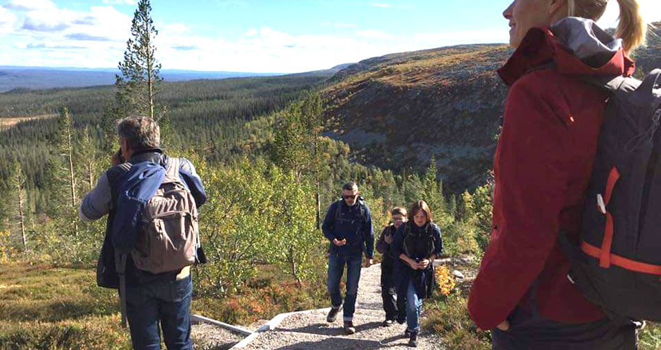 En grupp människor vandrar upp för en kulle med storslagen landskap bakom. 