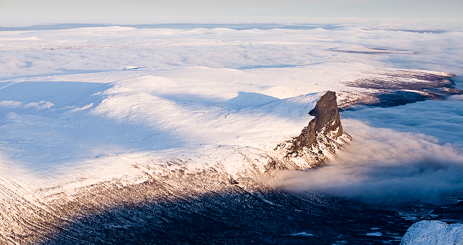 Utsikt från Skierffe. Man ser ett snöklätt Sarek. Solen lyser på toppen och snön. Man ser molnen som ligger i dalen från ovansidan.
