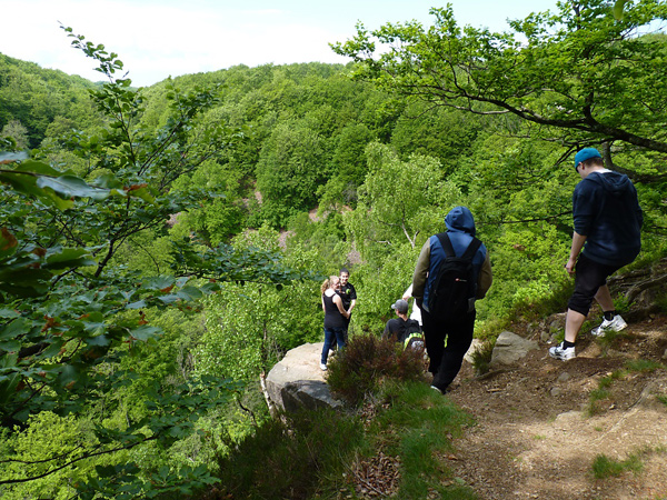 Lierna, utsiktspunkten där tre sprickdalar möts nedanför. Sommargrön skog och några ungdomar som står och beundrar utsikten