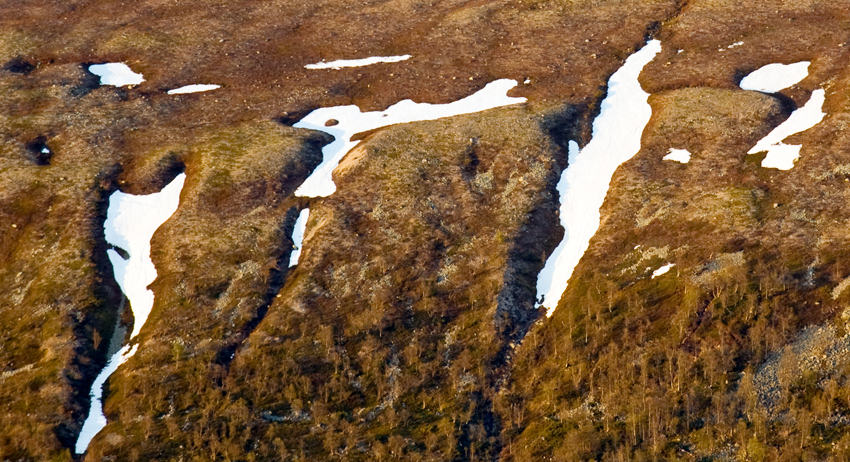 Flygfoto över bruna fjäll med skåror av snö.