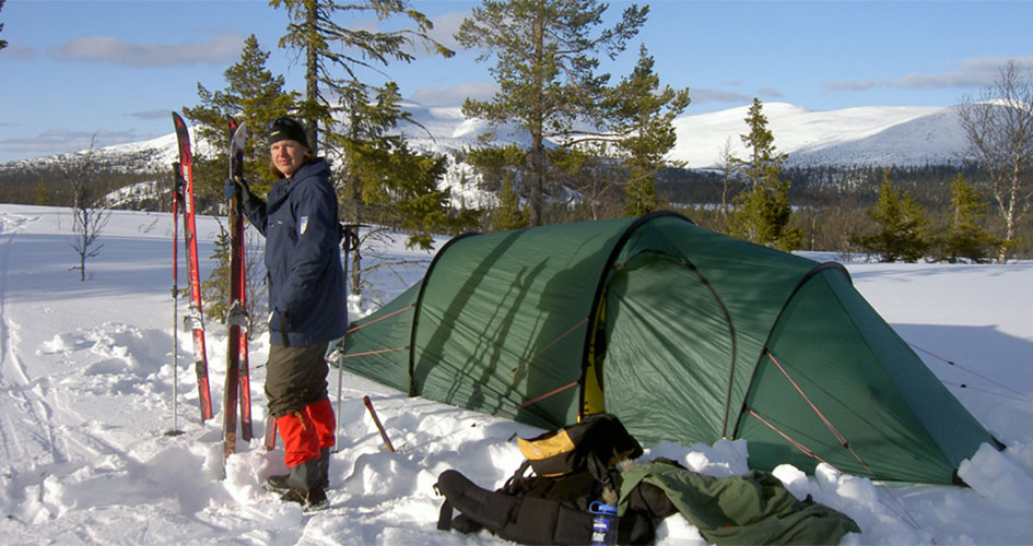 En person står bredvid sitt tält i snölandskap.