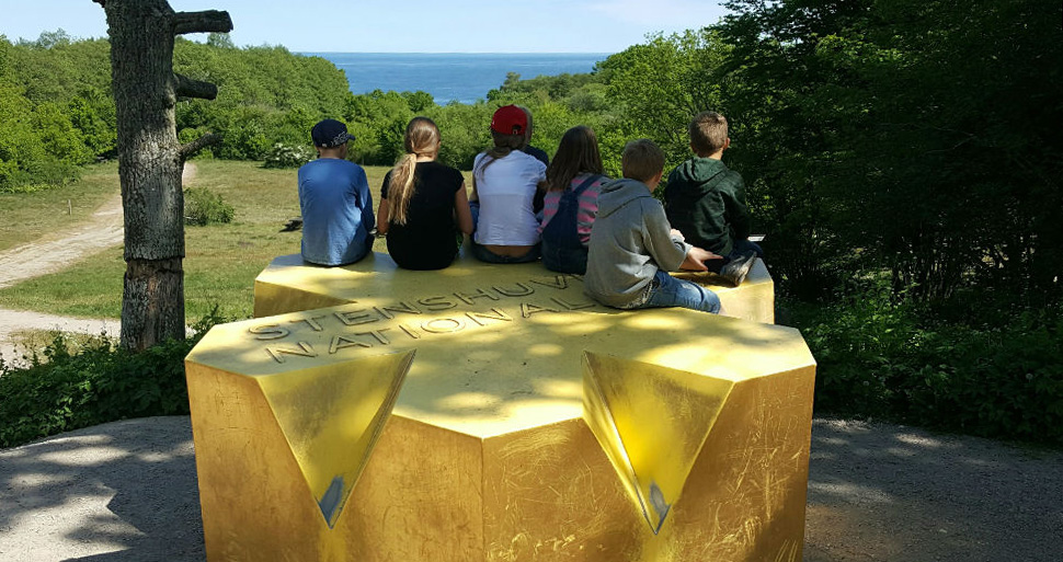 En del av en skolklass sitter på nationalparkens guldstjärna och tittar ut över havet i bakgrunden.