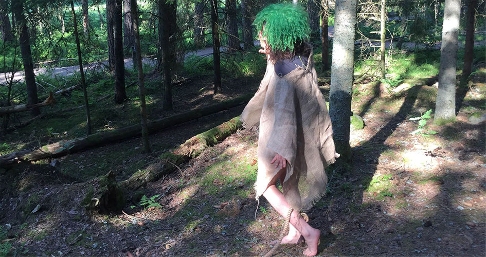 Utklädd till troll går ett barn med grönt hår går i skogen.