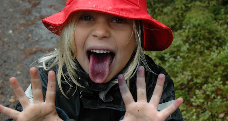 Ett barn med regnkläder sträcker ut tungan, som är blå av blåbär